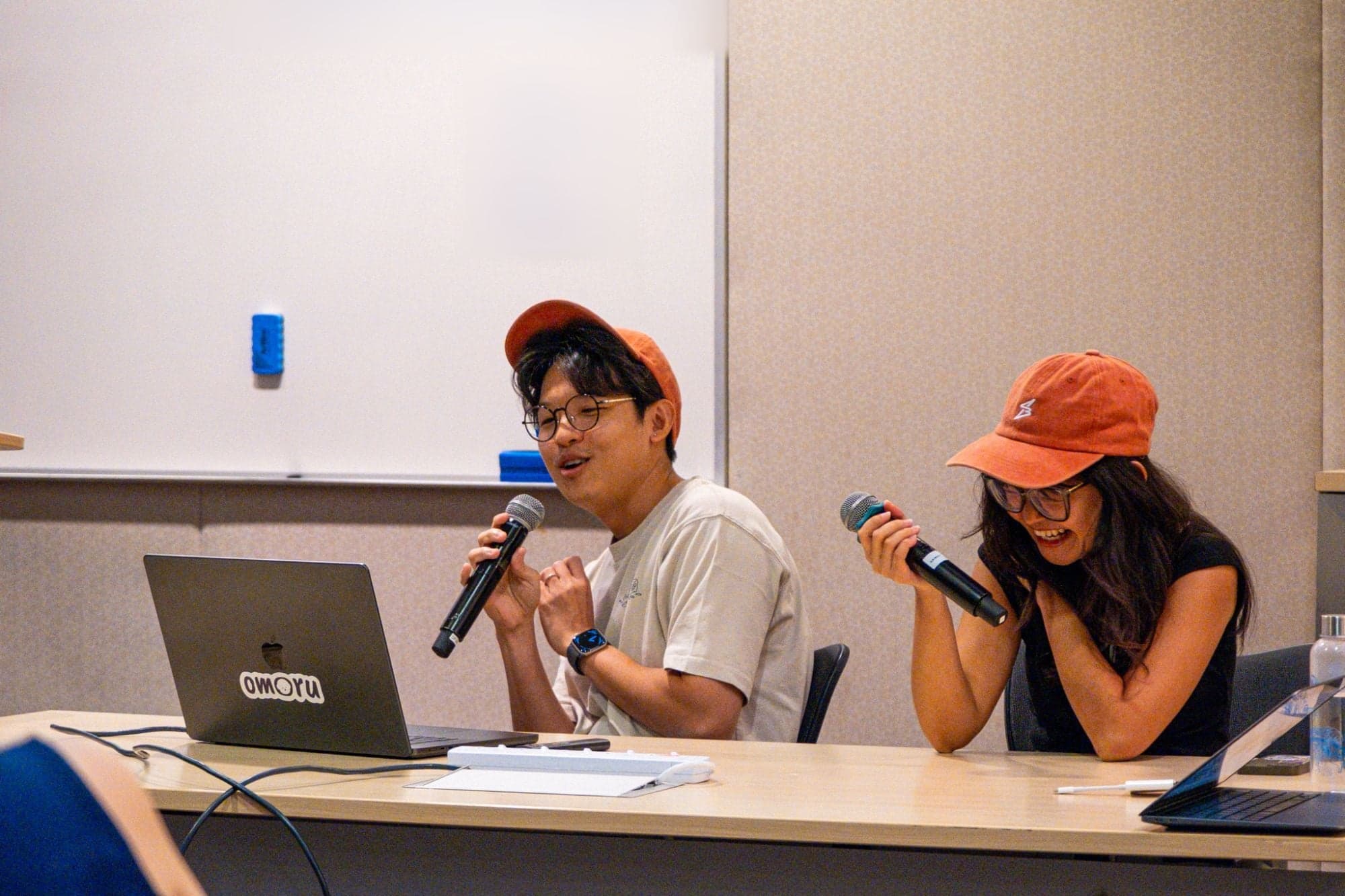 A large audience seated in rows of chairs, smiling and waving at the camera after the talk